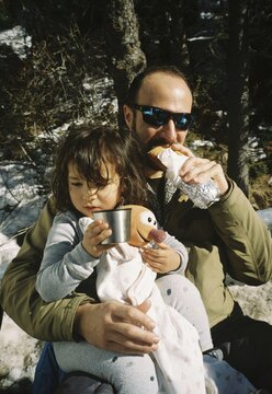 analog film photo of father and daughter having pic nic outdoors, eating sandwich outdoors on a sunny day, happy memories