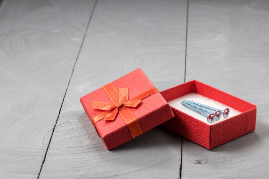 Red gift box revealing three metal screws, thoughtful gift for DIY and construction