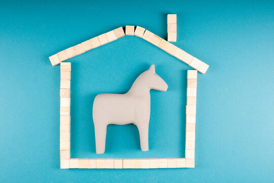 Toy horse trapped inside picture frame shaped as house, domestic limitation and security theme