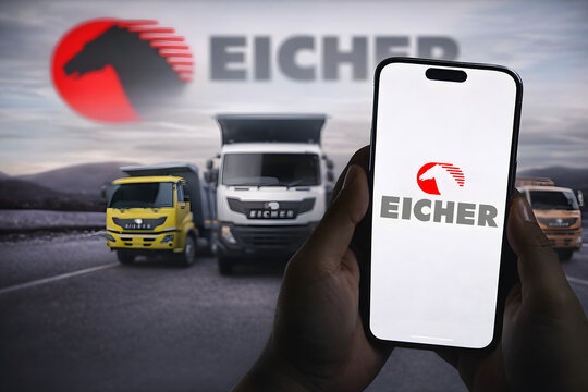 Eicher Motors logo on smartphone with trucks driving on road and Eicher branding in background, Indian commercial vehicle manufacturer and automobile sector stock concept