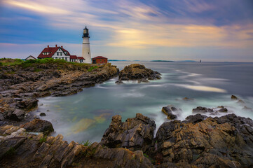 Fototapeta premium Sunset view of Portland Head Lighthouse overlooking rocky shoreline and calm ocean waters in Cape Elizabeth, Maine, USA. Long exposure.