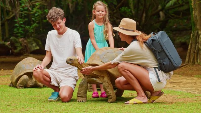 Family pet the head of a rare, giant turtle on the tropical island of Mauritius