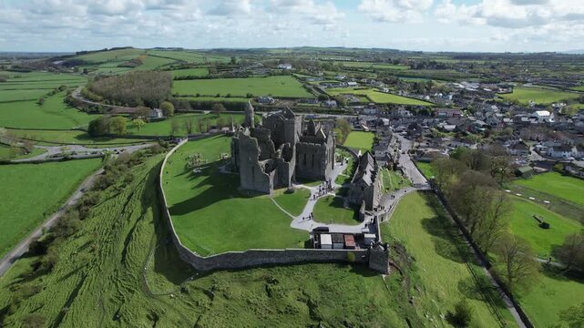 Aerial drone view of the Rock of Cashel, a historic medieval cathedral and fortress rising above the Irish countryside.