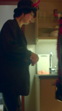 indoor doorway costume entrance, red devil with halo accessory and pet at feet, playful interaction with host in kitchen, festive evening atmosphere, candid hallway framing Vertical