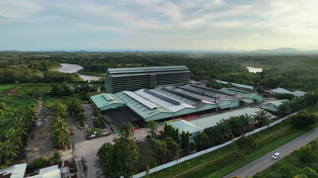 Aerial video of a factory complex surrounded by greenery, highways, and scattered buildings under a clear sky. Perfect for architectural, industrial, and environmental themes.