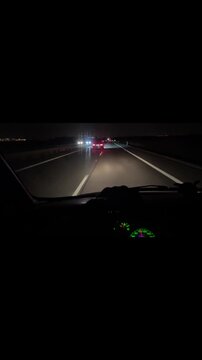 Night highway drive from dashboard, car headlights cutting darkness, taillights ahead, empty lanes and guardrail, tense motion and speed in long exposure vertical stock video