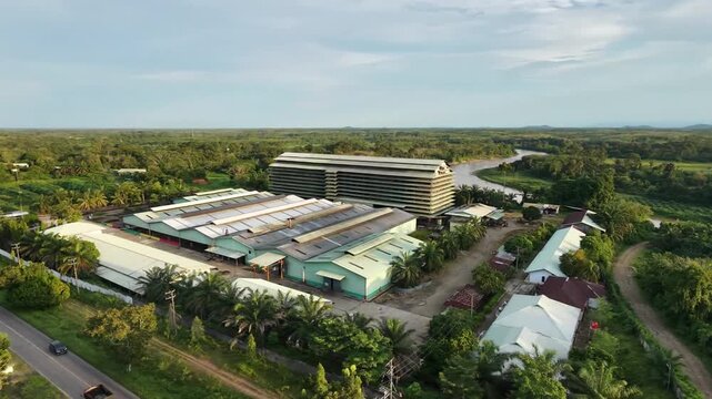 Aerial video of a factory complex surrounded by greenery, highways, and scattered buildings under a clear sky. Perfect for architectural, industrial, and environmental themes.