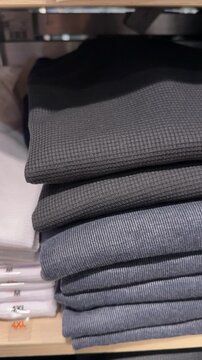 Stack of folded white t-shirts on display shelf with size labels visible in a retail store