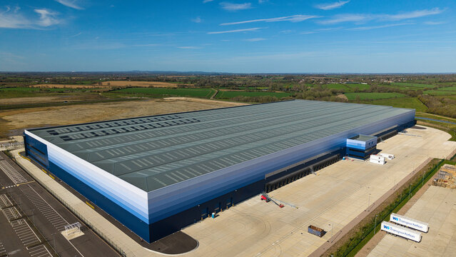 Aerial view of the large modern warehouse facility at Magna Park with blue gradient walls and extensive parking under a clear sky Magna Park, England, United Kingdom.