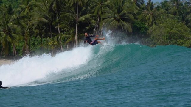 SLOW MOTION: Surfer launches into a powerful top turn on a breaking wave with palms and dense jungle in the background. Perfect surfing conditions at Beng Bengs surf spot in the tropical Mentawais.