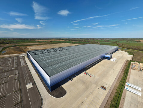 Aerial view of the massive warehouse facility at Magna Park with loading bays and parking areas under a blue sky in Magna Park, England, United Kingdom.