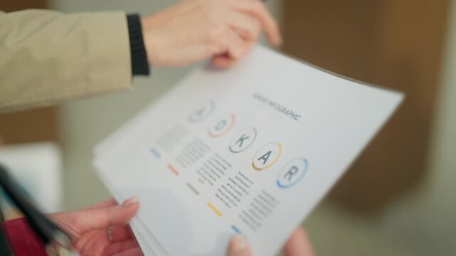 Hands of business people analyzing an info graphic document during a meeting. Two colleagues review data and information with a pen, pointing at key points.