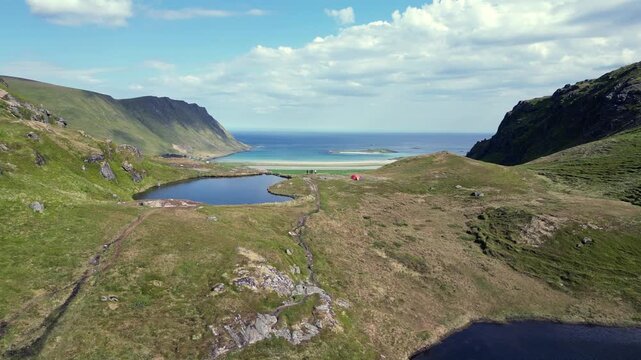 Stunning aerial view flying over the green valley and Lake Einangsvatnet, revealing the spectacular Kvalvika Beach in the Lofoten Islands