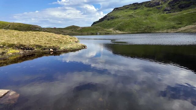Lake Einangsvatnet: Peaceful mountain lake with calm water reflecting the blue sky and clouds. Green grassy hills surrounding the scenic Nordic landscape. Lofoten islands.