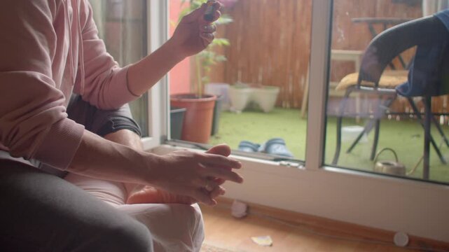 white man applying cream to feet near balcony, gently massaging heels and soles with lotion intimate selfcare moment after outdoor work, quiet domestic wellness routine.