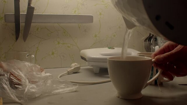 Man prepares warm drink, Individual pouring steaming water into cup in kitchen setting, Man carefully filling cup with hot water in cozy kitchen during morning routine