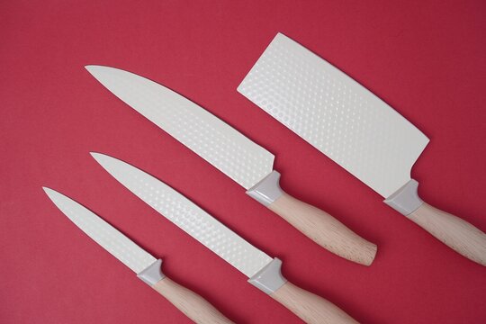 Top view of a professional chef knife set with white patterned blades and wooden handles arranged diagonally on a vibrant red background with copy space.