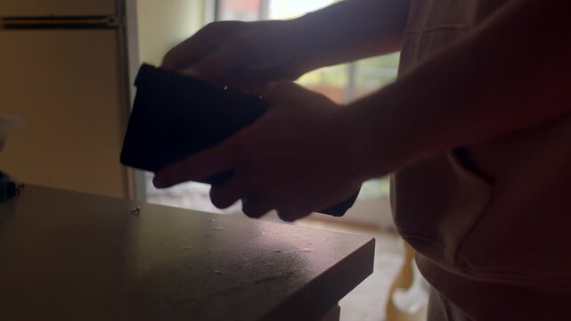 Man retrieves black bag, Caucasian man reaches for small black accessory on counter, Man with light skin picks up small black zippered pouch on counter in apartment setting