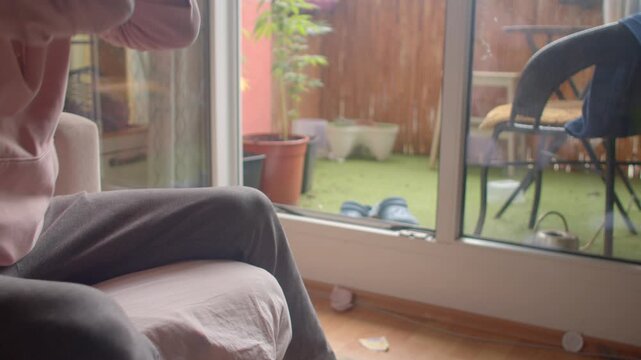 white man massaging aching foot and knee by balcony, wincing and applying pressure to sore area candid moment of discomfort and self treatment after strain or minor injury.