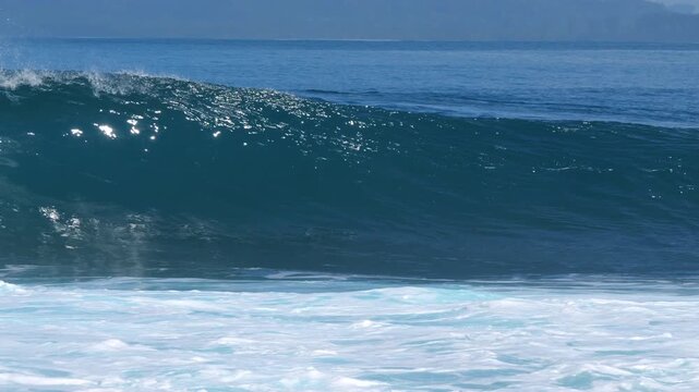 SLOW MOTION: Empty blue wave with offshore mist breaks along the shore as a small boat passes in the background near Ebay surf spot. Glassy tropical surf, sparkling water in the Mentawai Islands.