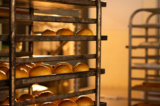 Commercial metal rack is holding trays of golden rolls in bakery, warm light is highlighting crusts