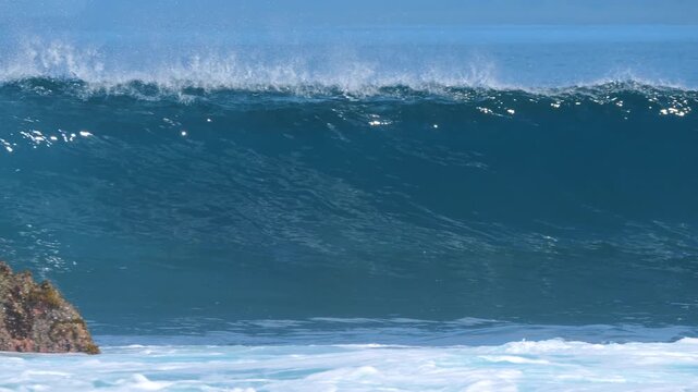 SLOW MOTION: Clean blue wave breaks beside a rocky outcrop at in the remote Mentawai Islands, Indonesia. Bright tropical light and a hollow reef break capture the raw beauty of firing wave conditions.