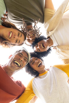 Diverse friends laughing, leaning together outdoors under bright sky with sunglasses and raglan tee