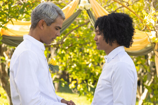 African American men ceremony cue standing holding hands under draped arch, showing boutonniere