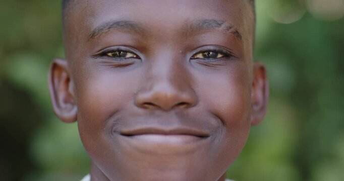 African teenage male smiling, shifting neutral face into broad grin at garden with green bokeh