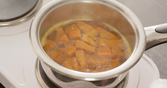 Heating stainless steel saucepan with orange veg pieces on white hob staying on, boiling to soften