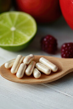 A wooden spoon filled with vitamin pills next to fresh fruit, perfect for a healthy snack or meal prep vertical frame