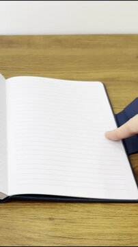 A close-up video, filmed vertically, showing a blue notebook being unpacked on a table.