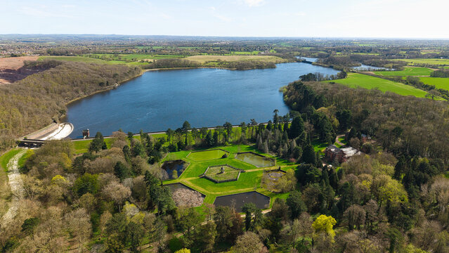 Aerial view of Swithland Reservoir featuring the dam wall, hexagonal ponds, and lush woodland under a clear spring sky in Leicestershire, England, United Kingdom.