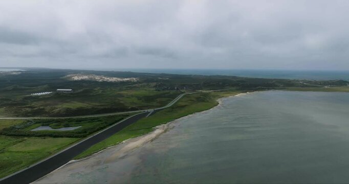 Aerial view of a road cutting through green landscapes alongside the calm water, creating a striking contrast of colors and textures, Sylt, Schleswig-Holstein, Germany.