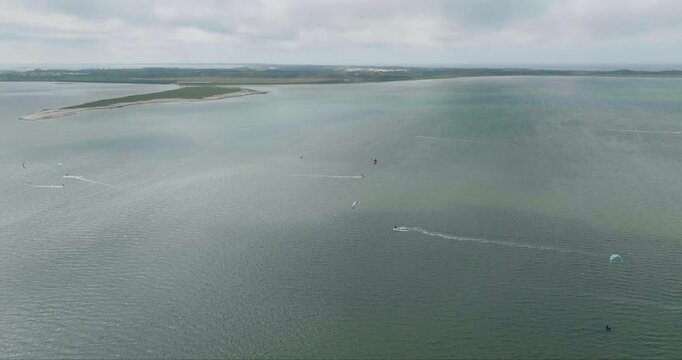 Aerial view of kitesurfers glide across the water under a cloudy sky, creating white wakes against the green-grey sea, Sylt, Schleswig-Holstein, Germany.
