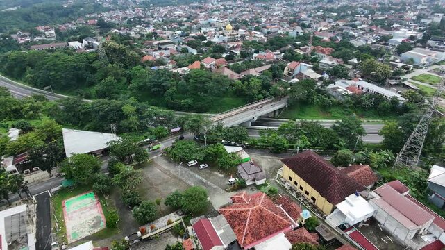 Aerial view of a densely populated residential area with lush green trees and a road bridge.