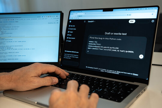 Milan, Italy 3/19/2026 Programmer hands typing on laptop keyboard using ChatGPT artificial intelligence software to find bugs in Python code with dual monitor setup for modern software development