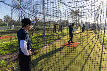 Naklejka premium Coach signaling, batter swinging during baseball practice in cage, animated lines showing bat path