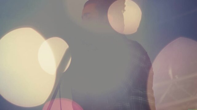 Vertical video: Lights cueing bearded singer in flannel singing into retro mic on stage with bokeh