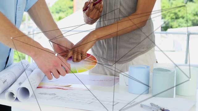 Designer shifting color wheel, pointing hue, partner tapping plan, aligning hue for plan under grid