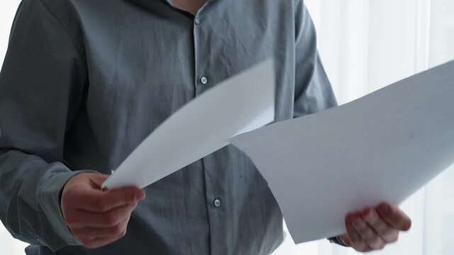 Office worker standing in a bright office while holding printed documents and reading assigned tasks, reviewing work instructions and information.