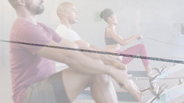 Middle man initiating drive while trio doing in-sync strokes on rowing machines for fitness class