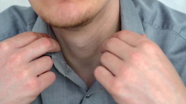 Close-up of a young man putting on a gray shirt and fastening buttons, preparing for work in a business office environment.
