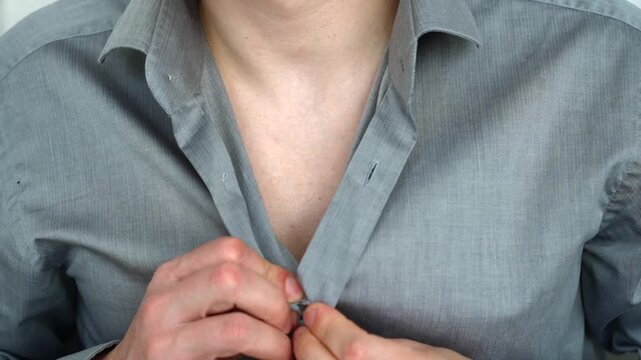 Close-up of a young man putting on a gray shirt and fastening buttons, preparing for work in a business office environment.
