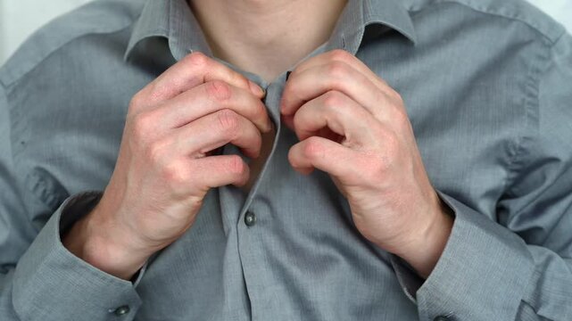 Young man wearing a gray shirt and buttoning it up, representing office dress code and professional appearance.