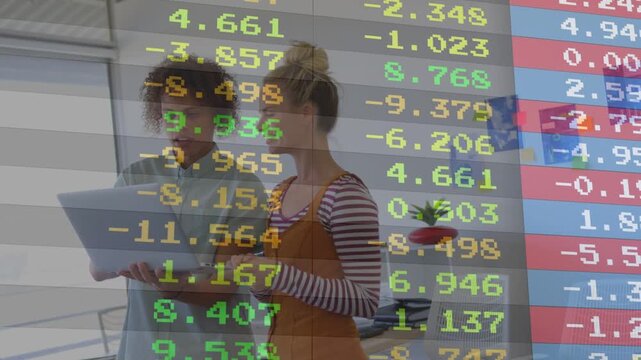 Two coworkers examining laptop and phone, leaning, pointing, reviewing market data overlay agreeing