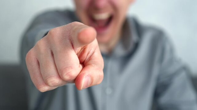 Man gesturing with his finger toward someone off-camera while laughing, expressing playful mockery and confidence in a light indoor setting.