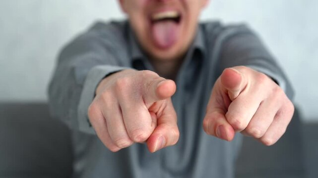 Young man in a bright room pointing toward the camera with a mocking smile, showing a teasing and provocative gesture. Concept of confrontation and social tension.