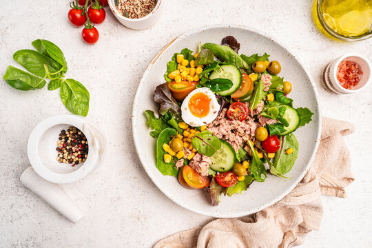Tuna salad with tomatoes, cucumber, corn, olives , eggs and onion on white stone background, top view. High quality photo
