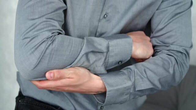 Close-up of a young male sitting and holding his sore elbow, expressing pain and limitation in movement. Concept of joint injury and strain.